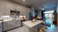 Located at 16304 FM-1325 in Round Rock, Texas, this single-story residence offers a thoughtfully designed interior with contemporary finishes throughout. The kitchen serves as a central highlight, featuring flat-front gray cabinetry, white quartz countertops, a decorative tile backsplash in a mixed gray pattern, stainless steel appliances including a range, microwave, dishwasher, and refrigerator, and a center island with bar seating — ideal for casual dining or entertaining. Light wood-look flooring runs through the kitchen and main living areas, contributing to a clean, cohesive aesthetic. The open layout connects the kitchen to the living space, which benefits from large windows that allow natural light to filter in. The bedroom is carpeted and features generous window placement, providing a bright and restful environment. The bathroom is finished with light wood-look flooring, a white quartz vanity, and a tiled tub-shower combination. A walk-in closet with built-in shelving and hanging space connects directly to the bathroom, offering practical storage. Overall, the space presents a modern, well-balanced interior with consistent finishes and functional design.