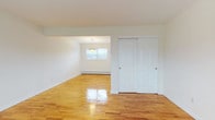This well-maintained, three-floor residence offers a clean and functional layout spread across its levels. Throughout the main living areas, warm-toned hardwood floors gleam underfoot, lending a cohesive and inviting character to the space. The main entry level welcomes you with a bright living area featuring a wide window that fills the room with natural light, along with a wall-mounted air conditioning unit and baseboard heating for year-round comfort. A staircase with a classic black iron railing connects the floors seamlessly.

The upper levels host generously sized bedrooms, each equipped with individual air conditioning units, baseboard heaters, and windows that bring in ample natural light. Sliding double-door closets provide practical storage. A pendant light fixture accents the dining area, adding a touch of warmth to the space.

The kitchen is outfitted with warm oak cabinetry, dark granite countertops, and white appliances including a gas range and over-the-range microwave, complemented by light wood-look flooring. The bathroom features tile flooring, a dark vanity with a white countertop, a shower with tile surround, and a window for ventilation.

The basement level offers substantial open space with a painted concrete floor and a dedicated laundry area with a washer and dryer, providing excellent utility and storage potential.