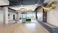 Located at 1400 Walnut St in the heart of Des Moines, Iowa, this thoughtfully designed amenity floor offers a generous footprint of interconnected spaces built for community, wellness, and leisure. The welcoming lobby lounge sets an immediate tone with its striking circular pendant lighting, a textured feature wall blending exposed brick and metallic finishes, and an eclectic mix of contemporary seating in rich greens and warm neutrals. Floor-to-ceiling windows pour natural light into the space while framing views of the outdoor courtyard beyond. Adjacent social areas feature reclaimed wood accent walls, dark hardwood flooring, and built-in banquette seating with Edison-style pendant lighting, creating intimate gathering spots ideal for casual interaction or focused work. A dedicated dining room with expansive glass walls and an exposed ceiling structure opens directly to the outdoor terrace, seamlessly blending indoor and outdoor living. The outdoor courtyard is generously sized for al fresco dining, lawn games, and relaxed socializing, surrounded by the building's warm wood and steel façade. The fully equipped fitness center rounds out the amenities, featuring a comprehensive selection of cardio machines, free weights, cable equipment, and medicine balls, all set atop vibrant patterned carpet with ample natural light from large windows.