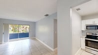 Located at 251 Bonnie Blvd in Palm Springs, Florida, this 2-bedroom, 1-bathroom single-floor home offers a practical and well-appointed layout with consistent light tile flooring and soft blue-gray walls throughout. The combined living and dining area is bright and open, anchored by a sliding glass door that leads to a private balcony overlooking lush greenery, filling the space with natural light and outdoor views. The kitchen has been updated with crisp white shaker cabinetry, granite countertops with subtle veining, and stainless steel appliances, including a range and over-the-range microwave. Both bedrooms are comfortably sized, each featuring windows that invite natural light—the primary bedroom offers a generous footprint with ample closet access, while the second bedroom provides a quiet retreat. The full bathroom is finished with large-format marble-look tile surrounding the tub and shower combination, paired with clean white fixtures for a fresh, modern feel. A hallway connects the rooms efficiently, and five closets distributed throughout the home provide notable storage capacity. Textured ceilings and clean white baseboards complete the interior aesthetic, giving the home a tidy, move-in-ready appearance.