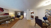 This single-floor residence offers a thoughtfully organized layout with distinct living, dining, kitchen, and sleeping areas. The living room serves as the focal point of the home, highlighted by a striking exposed brick accent wall that adds warmth and character to the space. Soft carpeting runs throughout, and a glass-top coffee table anchors the seating arrangement, creating an inviting atmosphere for relaxation or entertaining.

Adjacent to the living room, the dining area provides a dedicated space for meals, featuring a round glass-top table with upholstered chairs. Decorative wall art and a mirrored panel add visual interest, while a paneled entry door grounds the room.

The galley-style kitchen is efficiently designed with rich wood cabinetry, a butcher block-style countertop, a stainless steel sink, and wood-look flooring. Appliances including a refrigerator, range, dishwasher, and microwave are all integrated into the compact, functional layout.

The bedrooms are carpeted and comfortably sized, each offering natural light through windows with curtains. Closet space is generously provided, with large double-door closets visible in the bedroom areas, ensuring practical storage throughout the home. Textured ceilings are consistent across all rooms, contributing to the home's cohesive interior character.