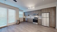 Located at Bear Creek Way NE in Redmond, Washington, this single-floor residence offers a clean, modern aesthetic throughout its thoughtfully designed layout. The open-concept living and kitchen area is anchored by a sleek, full-length kitchen featuring warm wood-tone cabinetry that extends floor to ceiling, providing generous storage. A geometric-patterned tile backsplash adds visual interest behind the countertops, which are finished in crisp white. A complete suite of stainless steel appliances — including a refrigerator, electric range, over-the-range microwave, and dishwasher — equips the kitchen for everyday use. Wood-look plank flooring runs seamlessly through the main living areas, lending warmth and continuity to the space. The living area is generously proportioned, bathed in natural light from large windows dressed with horizontal blinds, and finished with a ceiling fan. A sliding glass door opens to an outdoor access point, further enhancing the sense of openness. A dedicated walk-in storage closet provides additional organizational space off the main corridor. The bathroom is finished with large-format marble-look tile flooring, a wood-toned vanity with brushed nickel hardware, and a full walk-in shower, creating a clean and refined retreat.