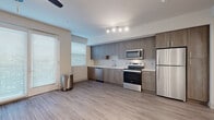 Located at Bear Creek Way NE in Redmond, Washington, this single-floor residence offers a clean, modern aesthetic throughout its thoughtfully designed layout. The open-concept living and kitchen area is anchored by a sleek, full-length kitchen featuring warm wood-tone cabinetry that extends floor to ceiling, providing generous storage. A geometric-patterned tile backsplash adds visual interest behind the countertops, which are finished in crisp white. A complete suite of stainless steel appliances — including a refrigerator, electric range, over-the-range microwave, and dishwasher — equips the kitchen for everyday use. Wood-look plank flooring runs seamlessly through the main living areas, lending warmth and continuity to the space. The living area is generously proportioned, bathed in natural light from large windows dressed with horizontal blinds, and finished with a ceiling fan. A sliding glass door opens to an outdoor access point, further enhancing the sense of openness. A dedicated walk-in storage closet provides additional organizational space off the main corridor. The bathroom is finished with large-format marble-look tile flooring, a wood-toned vanity with brushed nickel hardware, and a full walk-in shower, creating a clean and refined retreat.