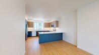 This contemporary three-story home offers a well-designed layout across three distinct levels. The ground floor houses a private attached garage with an automatic opener and an electrical panel, providing secure parking and convenient access to the home. Light wood-toned staircases with clean white railings connect each floor, contributing to the home's bright, modern aesthetic throughout.

The main living level features an open-concept kitchen and living area finished with light hardwood flooring. The kitchen is a standout space, equipped with stainless steel appliances including a refrigerator, microwave, and range. Bold navy-blue lower cabinetry is paired with warm wood-toned upper cabinets and crisp white countertops, anchored by a central island that adds prep space and a natural gathering point. Recessed lighting illuminates the space throughout.

The upper floors contain three bedrooms, three bathrooms, a hallway, and a closet. Bedrooms are finished with plush carpeting and feature large sliding windows that frame urban views, filling each room with natural light. The primary bedroom offers a comfortable, well-proportioned retreat. Bathrooms are finished in a clean, minimalist style with modern gray cabinetry. A dedicated closet provides additional storage. The home's consistent use of neutral tones, hardwood flooring, and recessed lighting creates a cohesive, move-in-ready environment.