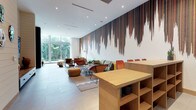This contemporary single-floor space makes a striking first impression with its dramatic statement wall mural — a cascading, multi-toned abstract design in earthy reds, browns, and blacks that commands attention across the entire length of the room. The high white ceilings, fitted with recessed lighting, amplify the sense of openness and allow the artwork to truly stand out.

The lounge area is thoughtfully furnished with an eclectic mix of mid-century modern and contemporary seating, including curved accent chairs in warm terracotta and leather tones, a low-profile sofa, and a woven pouf ottoman, all arranged around a patterned area rug that adds texture and warmth to the polished tile flooring. A wooden shelving unit with open compartments serves as a functional workspace or reception counter, adding a natural material contrast to the otherwise modern palette.

Floor-to-ceiling windows and sheer white curtains line the far wall, flooding the space with abundant natural light and offering unobstructed views of the lush tropical greenery outside. The seamless connection between the interior and the verdant outdoor landscape enhances the overall ambiance, creating a bright, welcoming, and design-forward environment ideal for gathering, working, or relaxing.