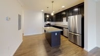 Located at 7525 Post Rd in North Kingstown, Rhode Island, this single-floor unit offers a well-designed layout with thoughtful finishes throughout. The kitchen is a standout feature, showcasing rich dark cabinetry, granite countertops, a central island with pendant lighting, and a full suite of stainless steel appliances including a refrigerator, range, microwave, and dishwasher. Wood-look flooring runs throughout the main living and kitchen areas, adding warmth and cohesion to the open-concept space. The living area is bright and spacious, with crown molding along the ceiling, multiple windows that invite natural light, and a door providing direct access to an outdoor balcony. The bedrooms are carpeted for comfort, each offering generous proportions and ample natural light through large windows, with closet access conveniently included. The bathroom features classic black-and-white hexagonal tile flooring paired with a dark vanity and white countertop, creating a clean, timeless aesthetic. A dedicated laundry area accommodates a stacked washer and dryer unit, adding practical convenience to the home. The overall ambiance is clean, modern, and move-in ready.