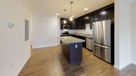 Located at 7525 Post Rd in North Kingstown, Rhode Island, this single-floor unit offers a well-designed layout with thoughtful finishes throughout. The kitchen is a standout feature, showcasing rich dark cabinetry, granite countertops, a central island with pendant lighting, and a full suite of stainless steel appliances including a refrigerator, range, microwave, and dishwasher. Wood-look flooring runs throughout the main living and kitchen areas, adding warmth and cohesion to the open-concept space. The living area is bright and spacious, with crown molding along the ceiling, multiple windows that invite natural light, and a door providing direct access to an outdoor balcony. The bedrooms are carpeted for comfort, each offering generous proportions and ample natural light through large windows, with closet access conveniently included. The bathroom features classic black-and-white hexagonal tile flooring paired with a dark vanity and white countertop, creating a clean, timeless aesthetic. A dedicated laundry area accommodates a stacked washer and dryer unit, adding practical convenience to the home. The overall ambiance is clean, modern, and move-in ready.