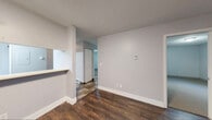 This single-floor unit at 405 Gaffney Drive in Watertown, New York, offers a straightforward and functional layout with a clean, neutral aesthetic throughout. The living area features rich, dark hardwood-style flooring and light gray walls accented by crisp white baseboards. A textured ceiling runs throughout the main living spaces, adding subtle visual depth. A pass-through window connects the living area to the kitchen, enhancing the open feel between the two spaces. The living room also benefits from a glass door that opens directly to a grassy outdoor area, allowing natural light to fill the room.

The kitchen is equipped with ample white cabinetry framed in wood-toned trim, generous counter space, a double stainless steel sink, a dishwasher, a coil-top electric range, and a refrigerator. Tile flooring grounds the kitchen area practically.

The bedrooms are carpeted for comfort and include baseboard heating units, with at least one bedroom featuring a window for natural light. The bathroom is well-appointed with a full tub and shower surround, a toilet, a single-sink vanity with a white countertop, and a large mirror. Stone-look tile flooring completes the bathroom's clean, functional design.