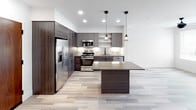 This contemporary single-floor residence at 1921 Union St in Anaheim, California, showcases a thoughtfully designed interior with modern finishes and a clean aesthetic throughout. The open-concept kitchen serves as a centerpiece of the home, featuring dark wood-grain cabinetry with matte black hardware, stainless steel appliances including a gas range, microwave, refrigerator, and dishwasher, along with a tile backsplash, under-cabinet lighting, open shelving, and a central island with pendant lighting above — ideal for both cooking and entertaining. Light wood-style flooring flows through the main living and kitchen areas, adding warmth and continuity. The bedrooms are carpeted for comfort and equipped with ceiling fans, natural light from windows, and access to closet space, providing a relaxed and functional retreat. The bathroom is finished in a modern style with wood-look tile flooring, a full soaking tub and shower combination with white subway tile surround, matte black fixtures, a dark vanity with a stone countertop, and a large mirror with contemporary lighting. The overall ambiance of the space is clean, minimal, and modern, making it a well-appointed home in the heart of Anaheim.