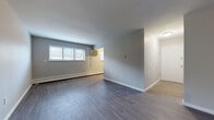 Located at 201 S Waverly Rd in Lansing, Michigan, this single-floor unit offers a clean, updated interior designed for comfortable everyday living. Durable vinyl plank flooring flows consistently throughout the space, lending a cohesive and contemporary feel to every room.

The open living area is generously proportioned, featuring neutral gray walls, bright windows with blinds that allow natural light to filter in, and baseboard heating for year-round comfort. A wall-mounted air conditioning unit provides convenient climate control. The layout transitions smoothly from the living area into additional rooms, guided by a well-lit entryway corridor with a crisp white door.

The kitchen is a standout feature, equipped with two-tone cabinetry in gray and blue-gray hues, a full suite of black appliances including a refrigerator and electric range, an under-cabinet range hood, and a double sink. Light countertops complement the bold cabinetry for a modern aesthetic.

The bedrooms are calm and functional, each featuring neutral-toned walls, natural window light, and ample floor space. The bathroom is elegantly appointed with large-format marble-look tile surrounding a full soaking tub, adding a touch of sophistication to the unit's practical design.