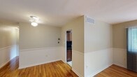 This single-floor space presents a clean, well-maintained interior with a thoughtfully designed layout. Warm hardwood flooring flows throughout the main living areas, lending a bright and inviting atmosphere that is further enhanced by natural light streaming through the windows.

The main living area features neutral, light-toned walls accented by classic chair-rail molding and substantial white baseboards, adding a touch of architectural detail to the space. A ceiling fan with a light fixture provides both comfort and illumination. A central HVAC vent ensures efficient climate control throughout.

An arched passageway connects the living area to the kitchen, which is outfitted with rich, dark wood cabinetry, dark stone countertops, and tile flooring — creating a functional and stylish cooking space that contrasts nicely with the lighter tones of the surrounding rooms.

A separate bedroom offers a serene retreat, complete with gleaming hardwood floors and a window that frames a lush, green outdoor view, filling the room with abundant natural light and a connection to the outdoors.

Overall, the space combines practical design with warm finishes, creating a comfortable and versatile environment suitable for a variety of uses.