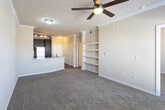 This single-floor residence at 5801 Deauville Blvd in Midland, Texas offers a well-appointed, cohesive layout designed for comfortable everyday living. The kitchen serves as a central highlight, featuring rich dark-espresso cabinetry, granite-style countertops, a subway tile backsplash, and a full suite of stainless steel appliances including a range, microwave, dishwasher, and refrigerator. Warm wood-style flooring grounds the kitchen area, while a peninsula with a double sink connects the space seamlessly to the living area. The living room is finished with crown molding, a ceiling fan, and plush carpeting, creating a warm and inviting atmosphere. Natural light filters in through windows with blinds, brightening the space throughout the day. A charming bay window alcove in one of the bedrooms adds architectural interest and additional natural light. The bedroom also offers direct access to a private bathroom, which includes dark cabinetry with granite-style countertops, a large vanity mirror, wood-style flooring, and a shower. Built-in shelving provides additional storage solutions within the unit. Crown molding detail is carried consistently throughout the living spaces, lending a polished, finished look to the overall interior.