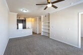 This single-floor residence at 5801 Deauville Blvd in Midland, Texas offers a well-appointed, cohesive layout designed for comfortable everyday living. The kitchen serves as a central highlight, featuring rich dark-espresso cabinetry, granite-style countertops, a subway tile backsplash, and a full suite of stainless steel appliances including a range, microwave, dishwasher, and refrigerator. Warm wood-style flooring grounds the kitchen area, while a peninsula with a double sink connects the space seamlessly to the living area. The living room is finished with crown molding, a ceiling fan, and plush carpeting, creating a warm and inviting atmosphere. Natural light filters in through windows with blinds, brightening the space throughout the day. A charming bay window alcove in one of the bedrooms adds architectural interest and additional natural light. The bedroom also offers direct access to a private bathroom, which includes dark cabinetry with granite-style countertops, a large vanity mirror, wood-style flooring, and a shower. Built-in shelving provides additional storage solutions within the unit. Crown molding detail is carried consistently throughout the living spaces, lending a polished, finished look to the overall interior.
