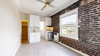 Located at 5014 Melrose Ave in the heart of Los Angeles, this compact studio offers a thoughtfully arranged layout comprising a main living area, kitchen, bathroom, and closet — all on a single floor. The main living space is defined by light grey wood-look flooring, crisp white crown molding, and a ceiling fan with lighting, giving the room an airy, well-finished feel. A striking exposed brick accent wall adds warmth and a touch of industrial character, contrasting beautifully with the neutral, light-toned walls throughout.

The kitchen is efficiently designed with white shaker-style cabinetry extending floor to ceiling, providing ample storage. It features a stainless steel sink, tile backsplash, a compact gas range, and a mini refrigerator — all seamlessly integrated. The closet, accessible directly from the kitchen area, offers additional storage and utility.

The bathroom is bright and clean, appointed with white subway tile walls, a glass-enclosed tub and shower combination, hexagonal mosaic floor tile, and a marble-look countertop vanity with an undermount sink. A frosted window brings in natural light while maintaining privacy, enhancing the fresh, spa-like atmosphere. Overall, the space balances classic architectural details with modern finishes throughout.
