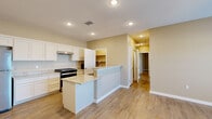 This single-story home offers a thoughtfully arranged floor plan encompassing three bedrooms, two bathrooms, a combined kitchen and living area, and a dedicated pantry closet. Wood-look tile flooring runs consistently throughout the entire home, providing a cohesive and low-maintenance aesthetic.

The kitchen is a standout feature, equipped with white shaker-style cabinetry, light granite countertops, stainless steel appliances including a refrigerator and gas range, and a peninsula with a built-in sink. A walk-in pantry closet directly off the kitchen provides generous storage. Recessed lighting illuminates the space effectively.

The primary bedroom is generously proportioned, offering ample room for large furnishings, and connects to the hallway through clean, white-trimmed doorways. The secondary bedrooms are comfortably sized with neutral walls and natural light from windows fitted with blinds.

The bathrooms continue the home's consistent design language, featuring granite vanity tops and wood-look tile flooring. One bathroom includes an accessible roll-under vanity, grab bars, and a walk-in tiled shower with a pebble-stone floor, a decorative mosaic accent border, and a built-in niche.

Throughout, warm neutral wall tones and consistent flooring create a unified, functional living environment.