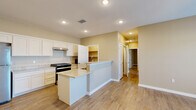 This single-story home offers a thoughtfully arranged floor plan encompassing three bedrooms, two bathrooms, a combined kitchen and living area, and a dedicated pantry closet. Wood-look tile flooring runs consistently throughout the entire home, providing a cohesive and low-maintenance aesthetic.

The kitchen is a standout feature, equipped with white shaker-style cabinetry, light granite countertops, stainless steel appliances including a refrigerator and gas range, and a peninsula with a built-in sink. A walk-in pantry closet directly off the kitchen provides generous storage. Recessed lighting illuminates the space effectively.

The primary bedroom is generously proportioned, offering ample room for large furnishings, and connects to the hallway through clean, white-trimmed doorways. The secondary bedrooms are comfortably sized with neutral walls and natural light from windows fitted with blinds.

The bathrooms continue the home's consistent design language, featuring granite vanity tops and wood-look tile flooring. One bathroom includes an accessible roll-under vanity, grab bars, and a walk-in tiled shower with a pebble-stone floor, a decorative mosaic accent border, and a built-in niche.

Throughout, warm neutral wall tones and consistent flooring create a unified, functional living environment.
