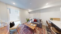 This thoughtfully designed single-floor residence blends modern aesthetics with functional living. The open-concept layout seamlessly connects the kitchen and living area, creating an inviting and cohesive space. The kitchen is a standout feature, anchored by a large island with a crisp white quartz countertop, dark cabinetry with brass hardware, and a gold-toned faucet. Pendant lights with brass accents hang above the island, adding warmth and style. A full suite of stainless steel appliances, including a refrigerator, microwave, and range, completes the kitchen. The living area offers a comfortable and well-lit retreat, with large windows that invite natural light and provide views of the surrounding exterior. Light hardwood flooring flows throughout, tying the spaces together with warmth and continuity. The bedroom is a serene and bright space, featuring a large window, recessed lighting, and clean white walls accented by framed artwork. The bathroom is finished in a clean, minimalist style with hexagonal tile flooring, a floating white vanity, a large mirror with bold black and brass light fixtures, and a glass-enclosed shower. Every detail of this residence reflects a commitment to contemporary design and comfortable urban living.