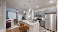 Located at 1720 Summit Crossing Lane in College Station, TX, this 1-bedroom, 1-bathroom unit offers a thoughtfully designed open-concept floor plan that maximizes every square foot of living space. Light wood-style flooring flows throughout, anchoring a cohesive and modern aesthetic.

The kitchen is a standout feature, showcasing gray shaker cabinetry, a granite countertop island with an undermount sink and seating for two, stainless steel appliances including a refrigerator, electric range, and microwave, plus recessed and pendant lighting overhead. The kitchen opens seamlessly into the living room, which is brightened by large windows with blinds and curtains, and includes a ceiling fan for added comfort.

The bedroom is a comfortable retreat with a window that allows natural light, wood-style flooring, a ceiling fan, and direct access to the bathroom and a dedicated closet. The full bathroom features a soaking tub with a tiled surround, wood-style flooring, and a walk-in closet with built-in shelving.

A dedicated laundry area with a stacked full-size washer and dryer adds everyday convenience. The unit's neutral color palette, clean lines, and functional layout make it a practical and attractive living space.