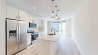 Located at 1601 Maguire Rd in Ocoee, Florida, this thoughtfully designed unit offers a bright, open-concept layout that seamlessly connects the kitchen and living room. Light-toned hardwood flooring flows throughout the main living areas, enhancing the airy, contemporary feel of the space.

The kitchen is a standout feature, showcasing white shaker cabinetry, stainless steel appliances including a French door refrigerator, electric range, and microwave. A central island with a quartz countertop and an undermount sink serves as both a prep space and a casual gathering spot, illuminated by stylish pendant lighting overhead.

The living area is filled with natural light, thanks to large sliding glass doors that open onto a private balcony overlooking the surrounding community. An additional window further brightens the space, creating a welcoming and open atmosphere.

The bathroom is finished with a clean, modern aesthetic, featuring a walk-in glass-enclosed shower with white tile surround and matte black hardware accents. The vanity includes granite countertops and white cabinetry, complemented by neutral stone-look tile flooring. A dedicated closet provides practical storage solutions to complete this well-appointed unit.