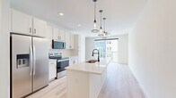 Located at 1601 Maguire Rd in Ocoee, Florida, this thoughtfully designed unit offers a bright, open-concept layout that seamlessly connects the kitchen and living room. Light-toned hardwood flooring flows throughout the main living areas, enhancing the airy, contemporary feel of the space.

The kitchen is a standout feature, showcasing white shaker cabinetry, stainless steel appliances including a French door refrigerator, electric range, and microwave. A central island with a quartz countertop and an undermount sink serves as both a prep space and a casual gathering spot, illuminated by stylish pendant lighting overhead.

The living area is filled with natural light, thanks to large sliding glass doors that open onto a private balcony overlooking the surrounding community. An additional window further brightens the space, creating a welcoming and open atmosphere.

The bathroom is finished with a clean, modern aesthetic, featuring a walk-in glass-enclosed shower with white tile surround and matte black hardware accents. The vanity includes granite countertops and white cabinetry, complemented by neutral stone-look tile flooring. A dedicated closet provides practical storage solutions to complete this well-appointed unit.