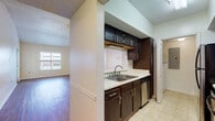 This well-appointed 2-bedroom, 2-bathroom residence is designed with functionality and comfort in mind across a single-story layout. The kitchen features dark espresso cabinetry with sleek hardware, light countertops, a double-basin sink, a stainless steel dishwasher, and black appliances including a refrigerator and range. A pass-through window opens the kitchen directly to the dining and living areas, enhancing the sense of openness throughout the common spaces. The dining area is highlighted by a classic chandelier and vaulted ceilings that amplify the feeling of spaciousness, while rich hardwood-style flooring flows through the living and dining areas, adding warmth to the interior. Natural light filters in through multiple windows, offering views of the surrounding exterior. Both bedrooms are generously sized, finished with plush carpeting, crown molding, and ceiling fans, creating a comfortable and quiet retreat. Each bedroom benefits from natural light through large windows with blinds. The bathrooms are clean and functional, featuring dark vanity cabinetry, light countertops, tile flooring, and a tiled tub-shower combination. The overall design balances practical features with a welcoming, neutral aesthetic throughout.