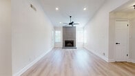 This thoughtfully designed single-floor home offers a bright, modern aesthetic throughout its two bedrooms and three bathrooms. Light hardwood flooring flows seamlessly across the entire space, complementing the crisp white walls and creating an airy, cohesive feel. The open-concept living and dining area serves as the heart of the home, anchored by a dramatic floor-to-ceiling tile fireplace flanked by large windows that invite abundant natural light. A ceiling fan overhead adds both comfort and style to the space. The kitchen is sleek and functional, featuring grey cabinetry, white quartz countertops, stainless steel appliances, and a classic white subway tile backsplash with dark grout for a contemporary contrast. The primary bedroom is generously sized and opens to a private balcony through sliding glass doors, offering pleasant outdoor views and its own ceiling fan. Each bedroom is equipped with closet storage, and the home includes three well-appointed bathrooms featuring grey vanities with white countertops and large-format tile surround tub-shower combinations. A dedicated laundry area and hallway complete the efficient, well-organized layout of this move-in ready home.