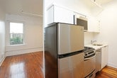 This single-floor unit combines classic character with modern updates, creating a comfortable and functional living space. Rich, warm-toned hardwood floors run throughout, adding timeless charm and a sense of continuity across every room.

The kitchen is efficiently designed and well-appointed, featuring stainless steel appliances including a gas range, over-the-range microwave, dishwasher, and refrigerator. White cabinetry and a clean white countertop provide ample storage and prep space, keeping the kitchen bright and organized.

The unit includes two open, light-filled rooms with white walls and gleaming hardwood floors. One room benefits from a double set of windows framing urban views of the surrounding cityscape, while the other features a single window with a classic cast-iron radiator beneath it — a nod to the building's historic character. Both rooms offer flexible use as living or sleeping areas.

The bathroom is clean and contemporary, finished with large white subway tiles surrounding a full soaking tub and shower combination. Chrome fixtures and white fixtures throughout maintain a crisp, cohesive aesthetic.

Natural light flows generously through multiple windows, enhancing the airy, open feel of the space. The combination of original hardwood floors, updated fixtures, and urban views makes this a well-balanced unit with both character and practicality.