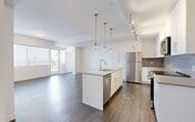 This well-appointed 2-bedroom, 2-bathroom unit at 10043 108 Street NW offers a thoughtfully designed open-concept layout with modern finishes throughout. The kitchen is a standout feature, showcasing floor-to-ceiling white cabinetry, a grey tile backsplash, stainless steel appliances, and a large central island with a quartz countertop and pendant lighting with gold accents. Track lighting adds additional functionality to the space. The kitchen flows seamlessly into the living room, which is bathed in natural light through expansive floor-to-ceiling windows offering sweeping city views. Dark hardwood-style flooring runs throughout the main living areas, complementing the clean white walls and modern aesthetic. The spacious primary bedroom features large windows with roll-down blinds and city views, while the second bedroom is equally well-lit with generous window coverage. Both bedrooms are finished with light hardwood-style flooring. The two bathrooms are finished with clean, contemporary fixtures — one featuring a soaker tub with a tiled surround, and the other a sliding glass-door shower — both with grey quartz vanity countertops and white cabinetry. The hallway provides ample built-in closet storage, completing this efficiently designed and stylish urban residence.