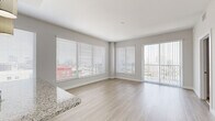This thoughtfully designed 2-bedroom, 2-bathroom residence offers a bright and modern living experience across a single floor. The open-concept living area is a standout feature, showcasing light wood-style flooring, neutral gray walls, and an abundance of natural light from large windows fitted with horizontal blinds. A sliding glass door leads to an outdoor balcony, offering elevated city views that extend into the bedrooms as well.

The kitchen is well-equipped with dark wood-grain cabinetry, granite countertops, a subway tile backsplash, and stainless steel appliances, including a range, microwave, and refrigerator. A peninsula with an integrated sink adds both workspace and a natural division between the kitchen and living area.

Both bedrooms are carpeted and generously sized, with the primary bedroom benefiting from a large window framing urban skyline views. Each bedroom is served by its own closet, including a walk-in closet with built-in shelving and hanging rods. The hallway connects all rooms efficiently, maintaining a practical and cohesive layout.

The bathrooms are finished with granite-topped vanities, dark wood cabinetry, framed mirrors, white tile flooring, and a tub-shower combination with tile surround. Clean lines and consistent finishes give the entire residence a polished, contemporary feel.