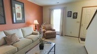 Located at 5535 Cabot Cove Drive in Hilliard, Ohio, this two-floor home offers a well-organized and comfortable layout designed for everyday living. The living room sets a warm and inviting tone with its distinctive terracotta accent wall, soft neutral carpeting, and a large window dressed with sheer grill-top curtains that allow generous natural light to fill the room. The space is thoughtfully proportioned, providing ample room for seating arrangements and relaxed gatherings. Subtle decorative touches, including framed wall art and accent lighting, contribute to the room's cozy yet polished ambiance. The neutral color palette used throughout the main living area creates a versatile backdrop that complements a variety of interior styles. Spanning two floors, the home offers distinct zones for living and private spaces, providing both functionality and a sense of separation between communal and personal areas. The overall design reflects a traditional residential aesthetic, balancing comfort and practicality. Situated in the established Hilliard community, this home benefits from a well-regarded suburban setting in central Ohio, making it a practical and appealing residence for a range of buyers or occupants.