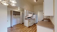 This single-floor residence offers a thoughtfully organized layout with a blend of hard-surface and carpeted flooring throughout. The galley-style kitchen is a functional highlight, lined with white cabinetry featuring wood-tone trim, laminate countertops, and white appliances including an electric range and refrigerator. A double-basin sink provides ample workspace, and the kitchen connects seamlessly to the rest of the home. Directly adjacent to the kitchen is a dedicated in-unit laundry closet, equipped with a full-size washer and dryer alongside an overhead storage shelf — a convenient and practical feature. The living and dining areas offer open, flexible space, with wood-look flooring transitioning to plush carpeting. A chandelier overhead adds a touch of warmth to the dining area. Both bedrooms are generously sized, carpeted for comfort, and each includes a sliding-door closet with built-in hanging rods. Large windows in each bedroom invite natural light and offer views of surrounding greenery. The bathrooms are clean and functional: one features a vanity with under-cabinet storage and a separate walk-in shower, while the other includes a full shower-tub combination. The overall ambiance is bright, neutral, and move-in ready.