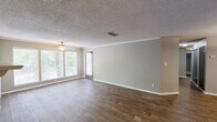 Located at 2000 Colony Park Dr in Birmingham, Alabama, this single-story, three-bedroom, two-bathroom home offers a well-organized layout with comfortable living spaces throughout. The open-concept living and dining area is a standout feature, showcasing wood-look flooring, crown molding, a textured ceiling, and a wood-burning fireplace with a white tile surround. Large windows along the front wall flood the living room with natural light and offer views of the surrounding mature trees. A pass-through connects the living area to the kitchen, which features gray cabinetry, light countertops, wood-look flooring, a double sink, and black appliances including a dishwasher and refrigerator. The spacious primary bedroom is carpeted and includes a louvered bi-fold closet, while additional bedrooms share similar finishes. Both bathrooms are consistently styled with gray vanities, stone-look countertops, wood-look tile flooring, and tub-shower combinations with white tile surrounds. A dedicated laundry area and walk-in storage with wire shelving add practical utility. An outdoor deck overlooks a tree-lined setting, providing a pleasant outdoor retreat. This home combines functional design with comfortable, move-in-ready finishes.