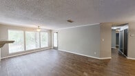 Located at 2000 Colony Park Dr in Birmingham, Alabama, this single-story, three-bedroom, two-bathroom home offers a well-organized layout with comfortable living spaces throughout. The open-concept living and dining area is a standout feature, showcasing wood-look flooring, crown molding, a textured ceiling, and a wood-burning fireplace with a white tile surround. Large windows along the front wall flood the living room with natural light and offer views of the surrounding mature trees. A pass-through connects the living area to the kitchen, which features gray cabinetry, light countertops, wood-look flooring, a double sink, and black appliances including a dishwasher and refrigerator. The spacious primary bedroom is carpeted and includes a louvered bi-fold closet, while additional bedrooms share similar finishes. Both bathrooms are consistently styled with gray vanities, stone-look countertops, wood-look tile flooring, and tub-shower combinations with white tile surrounds. A dedicated laundry area and walk-in storage with wire shelving add practical utility. An outdoor deck overlooks a tree-lined setting, providing a pleasant outdoor retreat. This home combines functional design with comfortable, move-in-ready finishes.