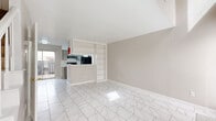 Located at 9430 Concourse Dr in Houston, TX, this two-story residence offers a thoughtfully laid-out 1-bedroom, 1-bathroom floor plan spread across two levels. The main floor features an open-concept living area finished with striking marble-look porcelain tile flooring that extends throughout, lending a bright and clean aesthetic to the space. The kitchen is positioned behind a half-wall pass-through with built-in open shelving, creating a functional divide while maintaining visual connectivity with the living area. The kitchen itself is galley-style, equipped with black appliances including a range, refrigerator, and dishwasher, complemented by gray cabinetry and a stainless steel sink. A sliding glass door on the main level provides access to an outdoor area and allows natural light to filter in. The upper level houses the generously sized primary bedroom, carpeted for comfort, with neutral warm-toned walls and ample room for furniture. A dedicated closet and a full bathroom are also found on this level. The bathroom features marble-look tile carried throughout — on the floors and extending up the walls of the tub/shower surround — alongside a vanity with gray cabinetry. The overall palette of warm grays and white finishes gives the home a clean, cohesive feel throughout.