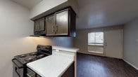 Located at 141 N Balcones Rd in Balcones Heights, Texas, this single-story unit offers a functional and straightforward layout designed for comfortable everyday living. The open-concept design connects the kitchen and living area seamlessly, creating an efficient use of space throughout.

The galley-style kitchen is well-equipped with dark espresso cabinetry featuring bar-pull hardware, speckled white countertops, a subway tile backsplash, and black appliances including an electric range, refrigerator, and under-cabinet range hood. A peninsular breakfast bar separates the kitchen from the living area, adding a casual dining option while maintaining the open feel of the shared space.

The living area features durable wood-style flooring in a dark tone and neutral gray walls that provide a clean, versatile backdrop. A ceiling fan with light kit keeps the space comfortable, and a front-facing window with blinds allows natural light to filter in alongside the entry door.

The bathroom includes a full tub and shower combination with white tile surround, a toilet, and a towel bar, all finished in a clean, minimalist style with wood-style flooring that coordinates with the rest of the unit. The overall ambiance is practical and move-in ready.