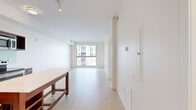 Located at 899 N Orange Ave in the heart of Orlando, FL, this one-bedroom, one-bathroom unit offers a well-organized layout across a single floor. The open-concept living and kitchen area is anchored by large windows that flood the space with natural light and offer views of the surrounding urban environment. Light-toned tile flooring runs throughout the main living area, enhancing the bright, airy atmosphere.

The kitchen is well-appointed with rich dark wood cabinetry, glass-panel upper cabinets, a light-colored backsplash, and a full suite of stainless steel appliances including a refrigerator, electric range, and microwave. A freestanding kitchen island with a wood frame provides additional prep and storage space, seamlessly connecting the kitchen to the living area.

The bedroom features plush carpeting, a large sliding window that brings in abundant natural light and urban views, and access to two closets, offering practical storage solutions.

The bathroom is clean and functional, finished with light tile flooring, a dark wood vanity with a white countertop, a tiled walk-in shower, and recessed lighting for a polished look.

Overall, the unit presents a modern, neutral aesthetic with a cohesive design language throughout, making it a practical and comfortable urban residence in downtown Orlando.