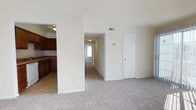 Located at 104 Dahlgren in Portsmouth, Virginia, this single-floor residence offers a practical and comfortable layout designed for everyday living. The open living area is finished with neutral-toned carpeting that extends throughout, creating a warm and cohesive feel across the main spaces. The kitchen is accessible via an arched doorway and is outfitted with rich, dark wood cabinetry, a double sink, a dishwasher, and tile flooring — providing a functional contrast to the carpeted living spaces. Ample upper and lower cabinet storage makes the kitchen well-suited for daily use. The main living area is bright and open, with neutral walls that lend a clean, move-in-ready aesthetic. A hallway extends from the living area, lined with a louvered closet door offering generous storage space, and leads toward additional rooms, including what appears to be a bedroom with a window allowing natural light to filter through. Overhead ventilation registers are present throughout, indicating a central HVAC system. The overall layout is straightforward and efficient, making good use of the available space on a single level. The home's understated design and neutral palette provide a versatile backdrop adaptable to a variety of furnishing styles.