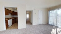 Located at 104 Dahlgren in Portsmouth, Virginia, this single-floor residence offers a practical and comfortable layout designed for everyday living. The open living area is finished with neutral-toned carpeting that extends throughout, creating a warm and cohesive feel across the main spaces. The kitchen is accessible via an arched doorway and is outfitted with rich, dark wood cabinetry, a double sink, a dishwasher, and tile flooring — providing a functional contrast to the carpeted living spaces. Ample upper and lower cabinet storage makes the kitchen well-suited for daily use. The main living area is bright and open, with neutral walls that lend a clean, move-in-ready aesthetic. A hallway extends from the living area, lined with a louvered closet door offering generous storage space, and leads toward additional rooms, including what appears to be a bedroom with a window allowing natural light to filter through. Overhead ventilation registers are present throughout, indicating a central HVAC system. The overall layout is straightforward and efficient, making good use of the available space on a single level. The home's understated design and neutral palette provide a versatile backdrop adaptable to a variety of furnishing styles.