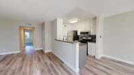 Located at 7240 Corbin Ave in Reseda, California, this single-floor unit offers a thoughtfully updated interior with a clean, modern aesthetic. The open-concept living and dining area is bathed in natural light from large sliding windows, with light wood-look flooring underfoot and a ceiling fan overhead that adds to the airy feel of the space. A peninsula-style kitchen is seamlessly integrated into the layout, featuring white shaker cabinetry, a dark mosaic tile backsplash, stainless steel appliances including a gas range, microwave, and refrigerator, and a dark-toned countertop that provides a stylish contrast. A hallway with recessed lighting connects the main living area to the private quarters. The two bedrooms are carpeted in a soft blue-gray tone and each benefit from large windows that bring in views of surrounding greenery. Two bathrooms serve the unit: one features a walk-in corner shower with frosted glass doors and a white vanity with dark countertop, while the second includes a full soaking tub and shower combination with matching white cabinetry. Textured ceilings are present throughout, and the neutral wall tones create a cohesive, move-in-ready environment.