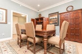 Located at 1485 Leverett Rd in Warner Robins, Georgia, this single-floor space offers a refined and welcoming environment with thoughtful architectural details throughout. The interiors are defined by soft sage-blue and neutral wall tones, crisp white crown molding, and light-toned tile flooring that flows consistently across the entire space, creating a cohesive and polished aesthetic.

A dedicated meeting or conference room serves as one of the primary functional areas, furnished with a rich cherry wood conference table surrounded by upholstered seating. Built-in wooden cabinetry and armoires line the walls, providing both storage and display space. Framed artwork and decorative accents add warmth to the room, while recessed lighting ensures a well-lit environment. An adjacent utility or prep area is accessible through a doorway, adding convenience to this workspace.

French doors connect the meeting room to an expansive open common area, which is bathed in natural light through large multi-pane windows dressed with wooden blinds and draped curtains. This grand open space features decorative columns, elegant pendant and chandelier lighting, and multiple comfortable seating arrangements. A fireplace anchors one end of the room, contributing to the inviting ambiance. The layout and finishes throughout suggest a professional yet comfortable setting well-suited for community gatherings or business use.