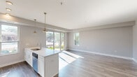 Located at 101 W Liberty St in Barrington, IL, this thoughtfully designed 2-bedroom, 2-bathroom residence offers a clean, contemporary aesthetic across a single floor. Consistent hardwood-style flooring and a neutral gray-and-white color palette create a cohesive, modern feel throughout the space.

The open-concept kitchen and living area serves as the heart of the home. The kitchen features white shaker cabinetry, quartz countertops, a large waterfall island with an undermount sink, stainless steel appliances, subway tile backsplash, and pendant lighting. Large sliding glass doors and windows flood the living area with natural light and provide views of the surrounding greenery.

Both bedrooms are well-proportioned, with the primary bedroom offering a spacious closet with white bi-fold doors and direct access to its en-suite bathroom. The primary bath is elegantly appointed with a dual-sink vanity, quartz countertops, white cabinetry, tile flooring, and a glass-enclosed walk-in shower with subway tile surround. The second bathroom mirrors this refined style with similar finishes.

A central hallway connects all rooms efficiently. The space benefits from abundant natural light, clean architectural lines, and contemporary finishes throughout, making it a polished and functional residence in downtown Barrington.