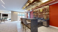 Located at 118 Park Ave in Rutherford, NJ, this sophisticated amenity space is designed to impress at every turn. The centerpiece of the space is a striking wet bar, anchored by a dramatic dark marble island with seating for multiple guests. Above, an elaborate ceiling installation of warm wood, burnished gold metalwork, and integrated LED lighting creates an unmistakable focal point, while open shelving lines the rich, deep-toned accent wall behind the bar.

The lounge area offers a refined retreat, featuring a modern fireplace set against stone tile cladding, a large wall-mounted television, and curated artwork that lends an art-forward sensibility throughout. Plush seating arrangements are anchored by vibrant, multicolored area rugs that contrast beautifully with the neutral palette of the carpeted floors and light-toned walls.

A billiards table anchors the central entertainment zone, while a separate conference area provides a sleek long table with upholstered seating and an additional wall-mounted screen—ideal for meetings or private events. Floor-to-ceiling windows and glass double doors flood the space with natural light and open directly to an outdoor terrace, seamlessly connecting the interior to the exterior. Large-scale artwork, including a vivid cityscape mural near the entry, adds a bold urban character throughout.