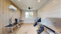 Located at 3272 State Highway 30 in Huntsville, Texas, this purpose-built dog grooming studio offers a clean, modern environment designed with both functionality and style in mind. The single-room space makes efficient use of its compact footprint, delivering a fully equipped grooming suite with a thoughtfully curated aesthetic.

The interior is defined by crisp white grid-pattern tile walls that line the majority of the space, complemented by warm wood-paneled accent walls that add contrast and a welcoming touch. A polished concrete floor with integrated floor drains ensures easy, hygienic cleanup — a practical necessity for a professional grooming environment. Recessed lighting and a sleek black ceiling fan provide comfortable, consistent illumination and climate control throughout, supported further by a wall-mounted mini-split HVAC unit.

The studio is equipped with multiple grooming tables and a stainless steel elevated bathing tub with integrated steps, allowing for efficient handling of dogs of various sizes. A glass door and a centrally positioned window flood the space with natural light and offer views of the surrounding outdoor area.

A glowing "Oh! My Dog" neon sign mounted on the wood accent wall adds a playful, branded personality to the space, rounding out a grooming studio that is as visually appealing as it is professionally appointed.