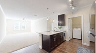 Located at 14746 Westbrook Cir in Bradenton, Florida, this single-story residence presents a well-designed open-concept layout that seamlessly connects the kitchen and living areas. The kitchen serves as a central focal point, featuring a large peninsula with light granite countertops, dark espresso cabinetry with brushed nickel hardware, and a suite of stainless steel appliances including a refrigerator, range, and microwave. Pendant lighting and track lighting illuminate the space, while crown molding adds a refined finishing detail throughout.

The living area extends naturally from the kitchen, offering generous open space with plush carpeting and a ceiling fan. Multiple carpeted bedrooms provide comfortable, quiet retreats, each with windows fitted with blinds that allow natural light while maintaining privacy. The bathroom continues the design language of the kitchen, featuring matching dark cabinetry, granite countertops, a large mirror, and hardwood-style flooring alongside a tub-shower combination. A dedicated laundry area houses a full-sized top-loading washer and dryer, adding practical convenience. The consistent use of neutral tones and quality finishes throughout creates a cohesive and functional living environment.