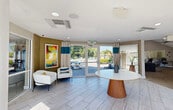 Located at 1735 Brantley Rd in Fort Myers, Florida, this single-floor community clubhouse offers a thoughtfully designed gathering space for residents. The interior spans a generous footprint and is organized into several distinct functional areas, each finished with modern, cohesive décor accented by teal and neutral tones throughout.

The welcoming entry lobby features large glass doors that frame views of the outdoor pool area, light-toned tile flooring, and a curved accent wall adorned with vibrant artwork. A round pedestal table anchors the space, while comfortable seating provides an inviting first impression.

The game and lounge room impresses with soaring double-height ceilings, oversized clerestory windows that flood the space with natural light, and ceiling fans. A billiard table serves as the centerpiece, complemented by plush seating and direct patio access.

The kitchen area is equipped with dark espresso cabinetry, granite countertops, a large central island with bar seating, stainless steel appliances, and a dedicated coffee bar station. Decorative columns add architectural character throughout.

Additional spaces include a cozy lounge with a tiled accent wall and wall-mounted TV, a bright leasing office with vaulted ceilings, and corridor seating nooks highlighted by a bold teal feature wall — creating an energetic yet comfortable community environment.