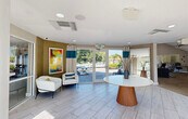 Located at 1735 Brantley Rd in Fort Myers, Florida, this single-floor community clubhouse offers a thoughtfully designed gathering space for residents. The interior spans a generous footprint and is organized into several distinct functional areas, each finished with modern, cohesive décor accented by teal and neutral tones throughout.

The welcoming entry lobby features large glass doors that frame views of the outdoor pool area, light-toned tile flooring, and a curved accent wall adorned with vibrant artwork. A round pedestal table anchors the space, while comfortable seating provides an inviting first impression.

The game and lounge room impresses with soaring double-height ceilings, oversized clerestory windows that flood the space with natural light, and ceiling fans. A billiard table serves as the centerpiece, complemented by plush seating and direct patio access.

The kitchen area is equipped with dark espresso cabinetry, granite countertops, a large central island with bar seating, stainless steel appliances, and a dedicated coffee bar station. Decorative columns add architectural character throughout.

Additional spaces include a cozy lounge with a tiled accent wall and wall-mounted TV, a bright leasing office with vaulted ceilings, and corridor seating nooks highlighted by a bold teal feature wall — creating an energetic yet comfortable community environment.