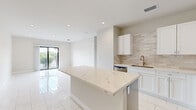 Located at 29 Palmetto Dr in Miami Springs, Florida, this two-bedroom, two-bathroom residence offers a clean, contemporary design with thoughtful finishes throughout. The open-concept living and dining area is bright and airy, with recessed lighting and large sliding glass doors that lead to a balcony overlooking lush greenery — bringing natural light and a tropical ambiance into the heart of the home.

The kitchen is a standout feature, showcasing a large center island topped with striking veined quartz countertops, white shaker cabinetry, a neutral tile backsplash, and a full suite of stainless steel appliances including a refrigerator, range, microwave, and dishwasher. Polished marble-look porcelain tile flooring flows seamlessly throughout the entire unit, contributing to a cohesive and upscale aesthetic.

Both bedrooms are well-proportioned, with the primary bedroom offering comfortable space, closet storage, and a window with views of the surrounding palm-lined neighborhood. The second bedroom is equally functional and bright. The two bathrooms are finished with decorative hexagonal marble-style tile flooring and clean white vanities, with windows that bring in natural light. The overall design palette — neutral whites, soft grays, and warm beige tones — creates a calm, modern atmosphere well-suited to South Florida living.
