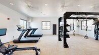 Located at 7430 N Silverbell Rd in Marana, Arizona, this fitness center offers a comprehensively equipped workout facility within a single, open-plan floor. The space is finished with light herringbone-patterned flooring and crisp white walls, creating a clean, modern aesthetic throughout.

The cardio zone features multiple treadmills, an Echelon rowing machine, a stationary upright bike, and a recumbent bike, several of which are equipped with interactive screens for on-demand workout programming. Large windows along the perimeter fill the room with natural light and offer views of the surrounding desert landscape, enhancing the workout environment.

At the center of the space stands a robust black functional training rig, outfitted with TRX suspension trainers, battle ropes, stability balls, medicine balls, and kettlebells organized on integrated storage racks. A dedicated cable machine and a full dumbbell rack provide additional strength training options. Ceiling fans are installed throughout to ensure airflow and comfort during workouts.

A motivational cycling-themed mural adds a dynamic visual accent to one wall, reinforcing the active atmosphere of the space. The layout is thoughtfully organized to allow users to move freely between equipment zones, making it suitable for a wide variety of fitness routines.
