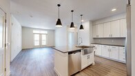 Located in Buda, TX, this well-appointed 2-bedroom, 2-bathroom residence offers a thoughtfully designed single-floor layout with a clean, modern aesthetic throughout. The open-concept kitchen and living area serves as the heart of the home, showcasing white shaker cabinetry, dark granite countertops, a central island with an undermount sink, and stainless steel appliances including a French door refrigerator, electric range, and built-in microwave. Three stylish pendant lights illuminate the island, complementing the recessed lighting overhead. Wood-style luxury vinyl plank flooring runs through the main living areas, adding warmth and continuity. The spacious living room is bathed in natural light from large windows and French doors that open to a private balcony overlooking the community. Both bedrooms feature plush carpet, ceiling fans, and generous natural light from wide windows. Each bedroom is paired with dedicated closet space, including a walk-in closet with built-in shelving and hanging rods. The bathrooms are finished with white vanity cabinetry, dark countertops, and a tiled tub-shower combination. The primary bath includes direct access to its walk-in closet, creating a functional and connected suite layout.