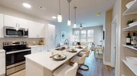 The Liza in North Little Rock, Arkansas offers a thoughtfully designed one-bedroom, one-bathroom residence that combines modern aesthetics with everyday functionality. The open-concept layout connects the kitchen, dining, and living areas seamlessly, creating an inviting and cohesive living space. The kitchen is a standout feature, showcasing sleek white cabinetry, quartz countertops, stainless steel appliances, and a spacious island with bar seating illuminated by elegant pendant lighting — ideal for both cooking and casual dining. Light wood-style flooring flows throughout the main living areas, complementing the bright, neutral color palette. The living room is generously sized and bathed in natural light from large windows, with a ceiling fan adding to the comfort of the space. A private door provides direct outdoor access from the living area. The bedroom is a calm retreat, featuring large windows that allow ample natural light and warm wood-toned flooring. The bathroom is finished with white cabinetry, quartz countertops, and brushed nickel fixtures, delivering a clean and polished look. Throughout the unit, modern design elements and quality finishes create a refined yet comfortable atmosphere well-suited for contemporary living.